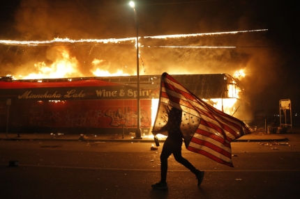 28일(현지시각) 경찰 과잉진압으로 인한 조지 플로이드의 사망에 항의하는 한 시민이 미국 국기를 들고 거리를 달리고 있다. 미니애폴리스/AP 연합뉴스